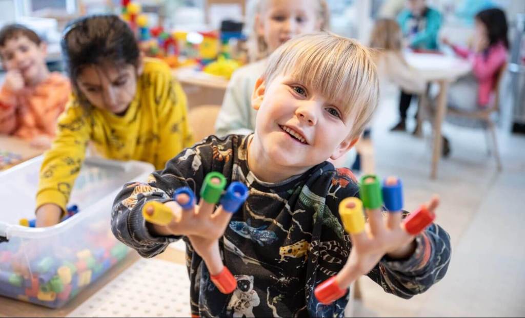 A young EC student smiling at some lego toys on their fingers.