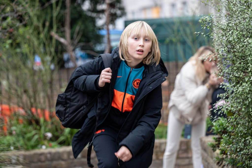 A young student with a Chelsea FC jacket and backpack on, leaving school
