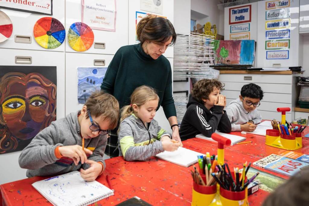 A teacher giving advice to 1 of 4 students as they do drawings in art class