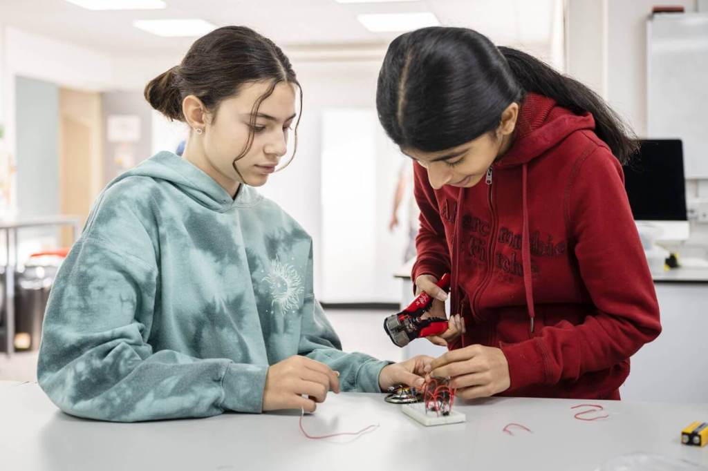 Two female students partaking in a science experiment involving wires and a speaker