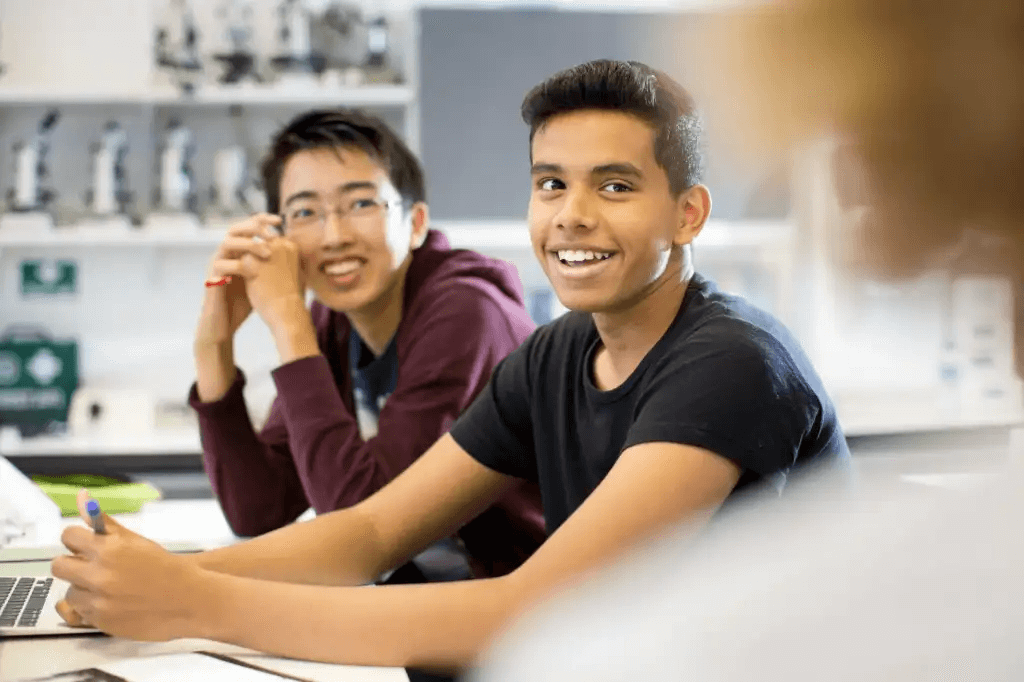 Two male students in class smiling while talking to their teacher